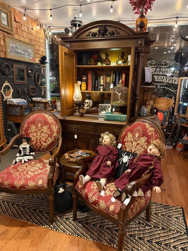 A seasonal Victorian display at Sassafras — damask armchairs in red and gold, an ornate armoire of collectibles, porcelain dolls, and string lights